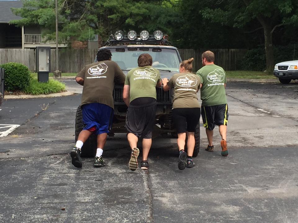 Four movers help push a stalled truck down the street