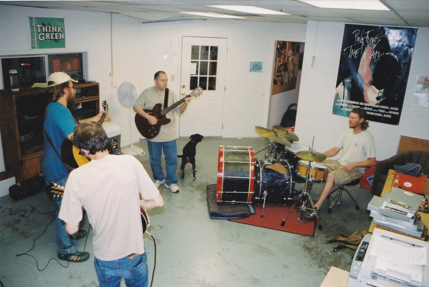 Some early Little Guys employees playing music in a jam room. Three guys are playing guitars and one is sitting at a drumset.