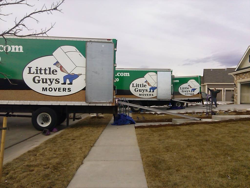 Little Guy posing next to three moving trucks