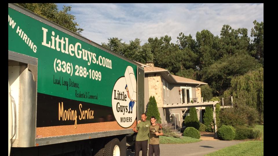 Two movers standing next to a moving truck, smiling and giving thumbs up
