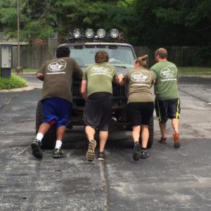 Four movers help push a stalled truck down the street