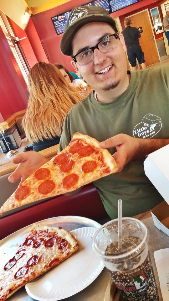 A Greensboro Little Guy holding a slice of pizza and smiling