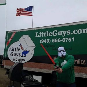 A Little Guys Movers holding a toy lightsaber and wearing a Star Wars helmet