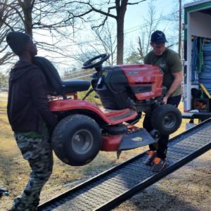 Two Little Guys Movers loading a tractor into a moving truck.