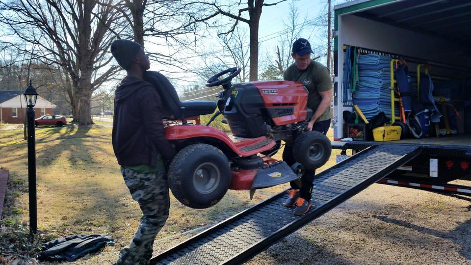 Two Little Guys Movers loading a tractor into a moving truck.