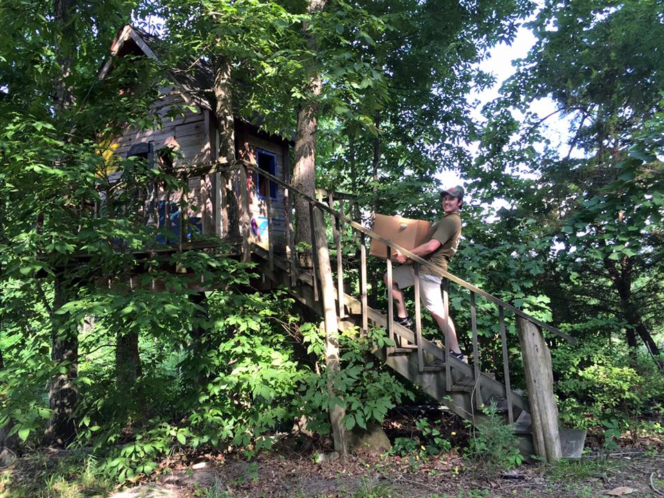 Mover carrying a box up the steps to a treehouse tucked in a wooded area