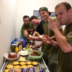 A group of Little Guys standing at a table filled with a bounty of cheeseburgers and sausages