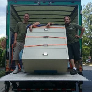 Two movers loading a filing cabinet into a moving truck.