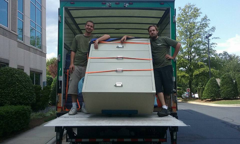 Two movers loading a filing cabinet into a moving truck.