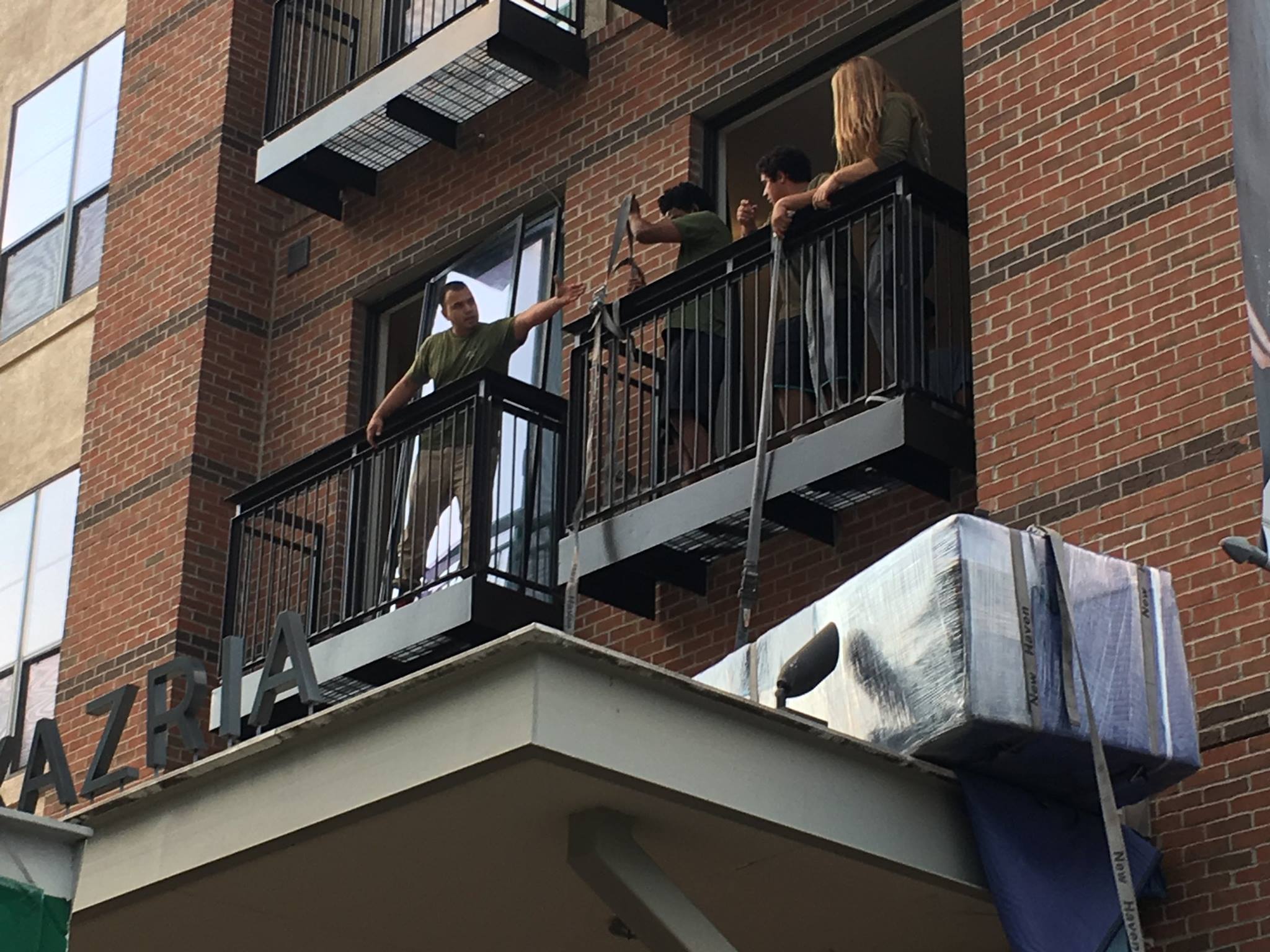 A crew moves a piece of furniture down a multistory building using the balcony
