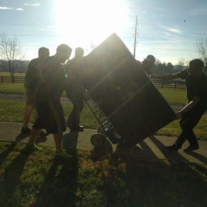 A crew working together to move a large piece of furniture on a dolly while the sun shines bright in the sky