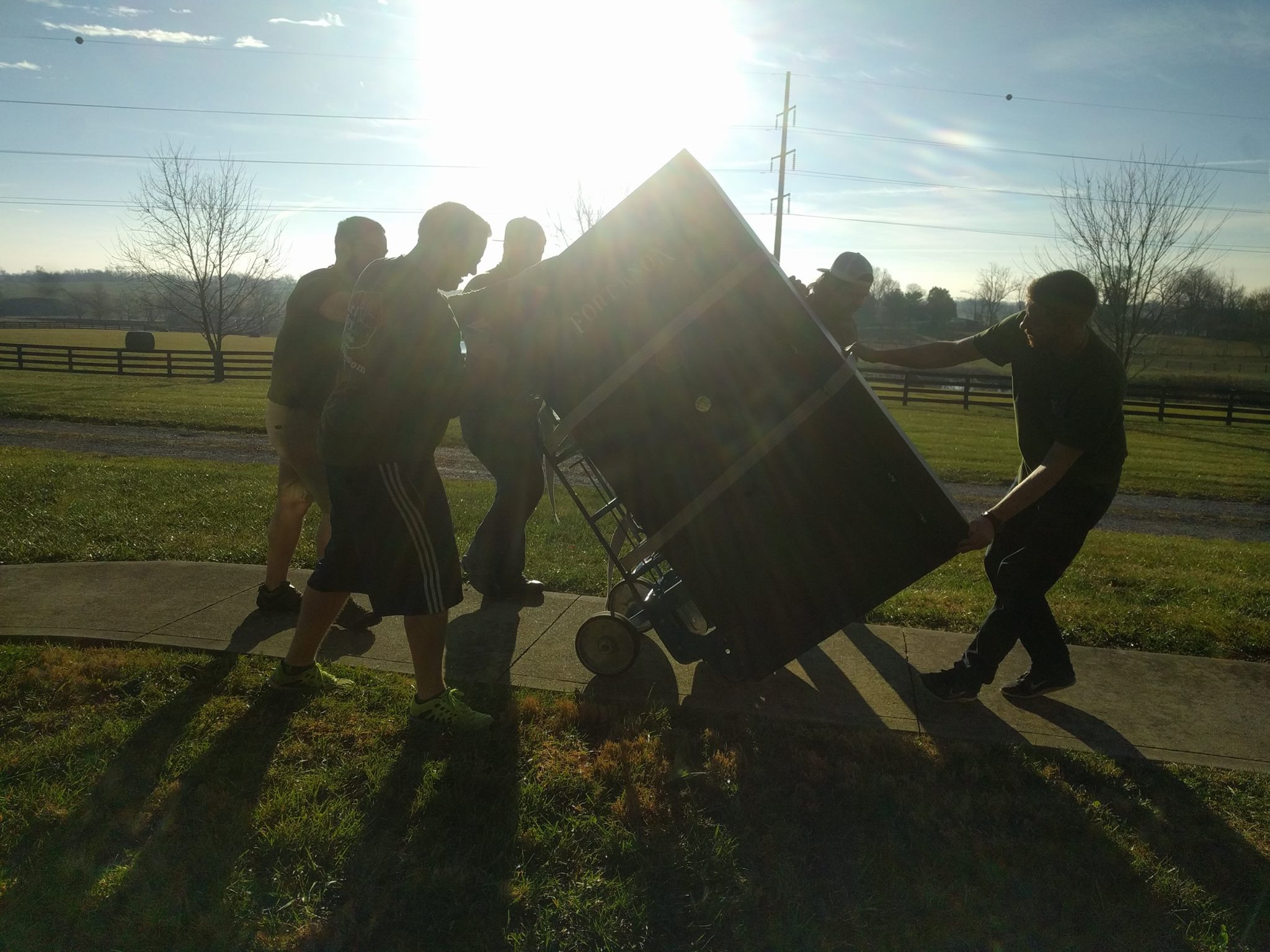 A crew working together to move a large piece of furniture on a dolly while the sun shines bright in the sky