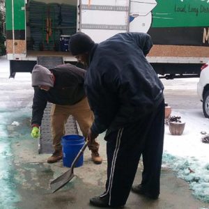 Two movers clearing a driveway of snow and ice to prepare for a move
