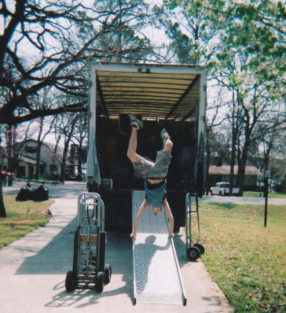 An old film photo of a mover doing a handstand on the ramp coming out of the back of the truck