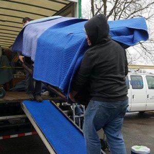 Two movers loading a piece of furniture wrapped in moving blankets into the truck