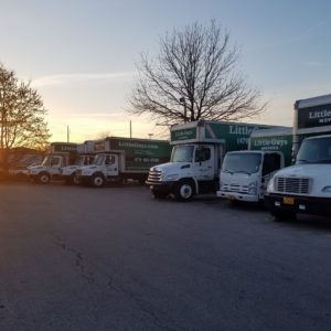 A row of Little Guys trucks in the shop parking lot at sunrise on a pleasant spring day