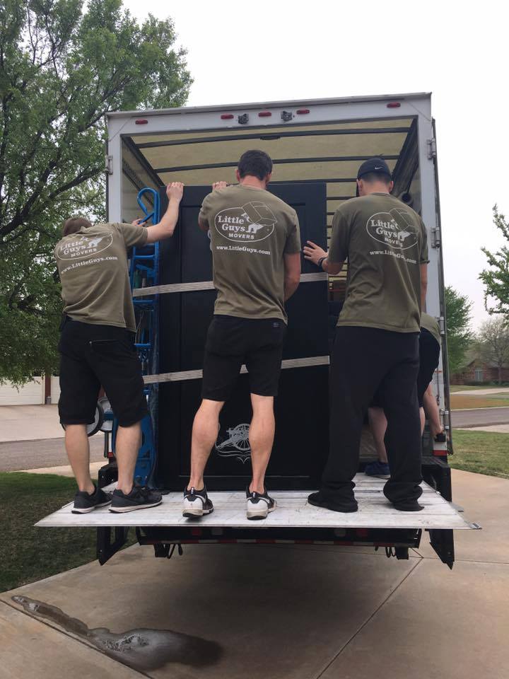 Four Little Guys Movers load a gun safe into a moving truck