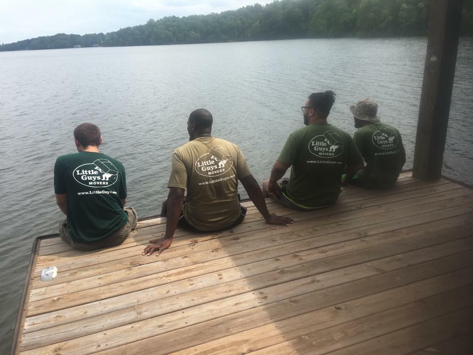 Four Little Guys movers sitting together on a dock overlooking a lake