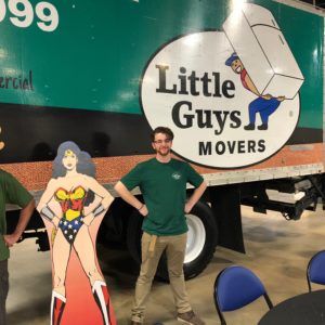 A Little Guy poses with a Wonder Woman cutout in front of a moving truck