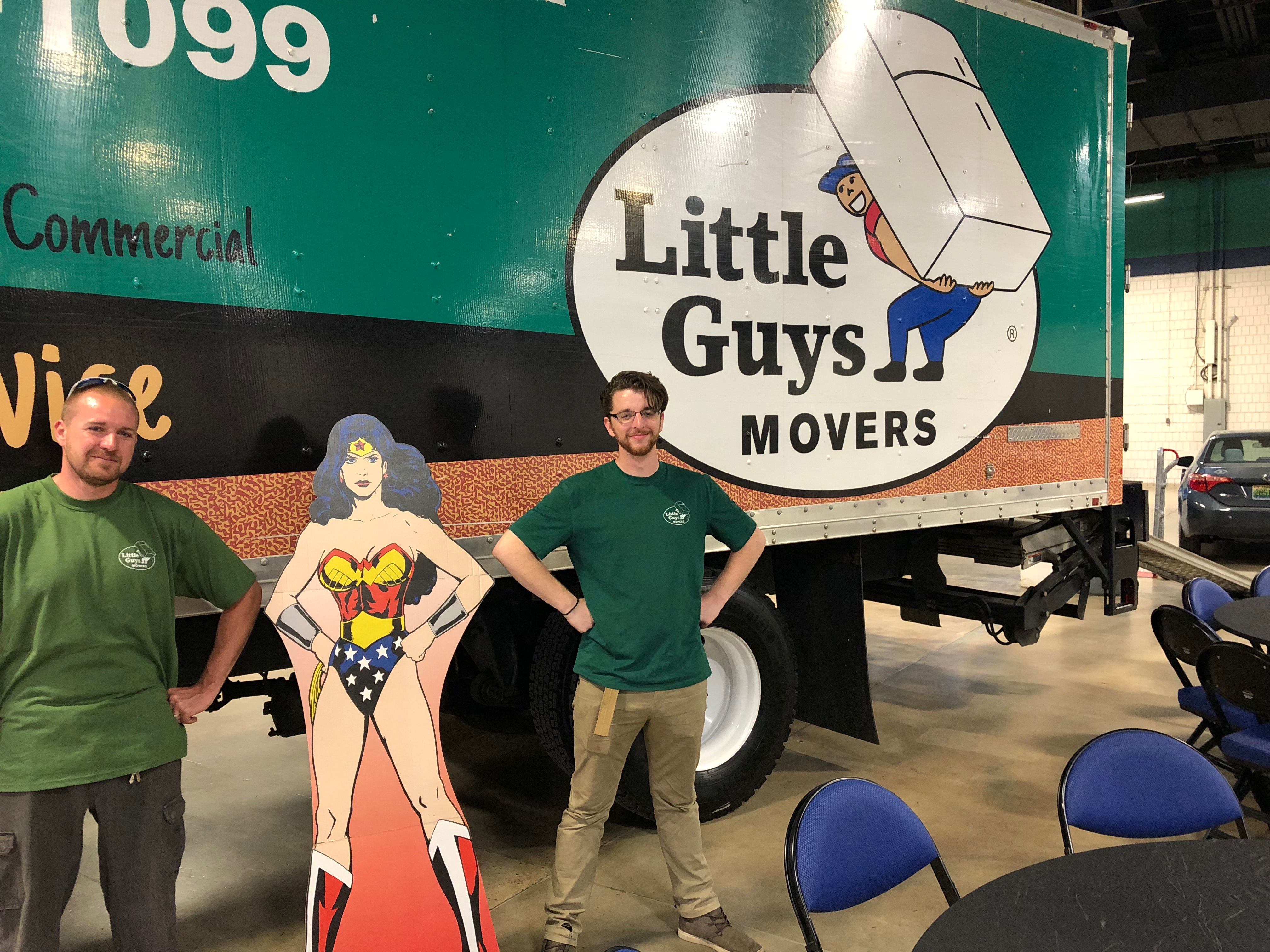 A Little Guy poses with a Wonder Woman cutout in front of a moving truck