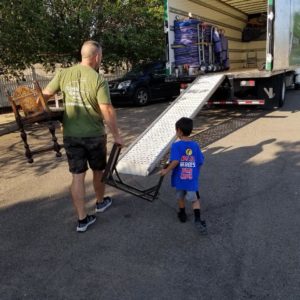 mover carrying a small table up the truck ramp with the help of a small boy