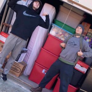two movers standing in front of norman storage units filled with boxes