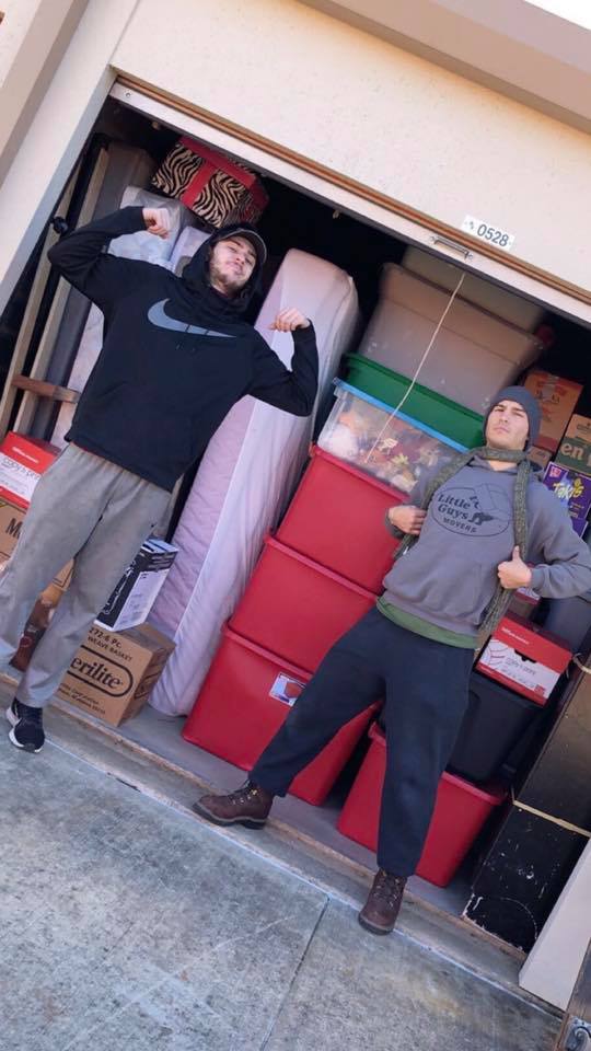 two movers standing in front of norman storage units filled with boxes