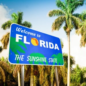 A beautiful "Welcome to Florida - The Sunshine State" sign in front of iconic palm trees