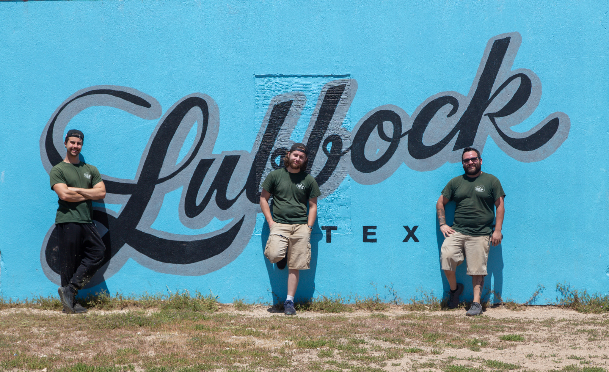 Three little guys employees in front of Lubbock mural in the arts district