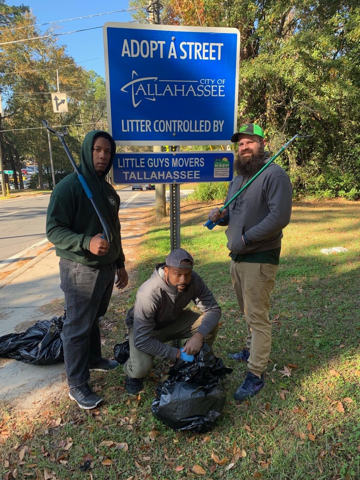 Three Tallahassee Little Guys Movers employees in front of Adopt a Street sign