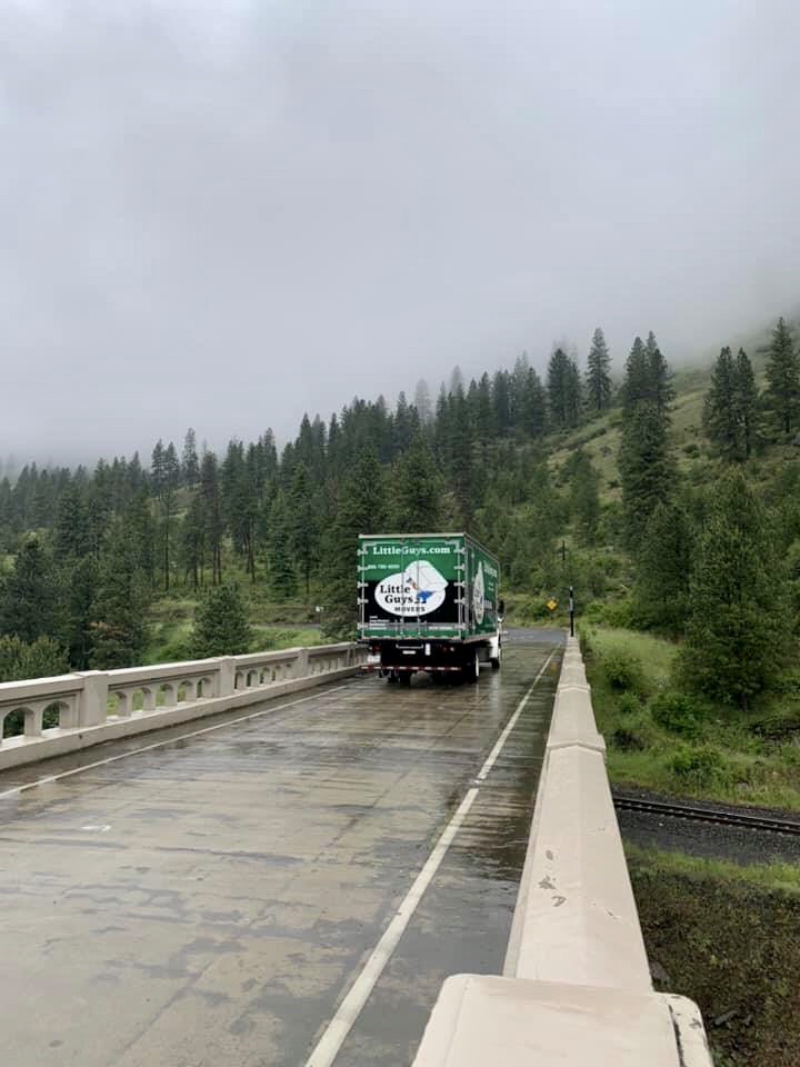 Little Guys Movers truck on road surrounded by forest