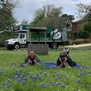 Two Little Guys Movers lay in a field of Texas bluebonnets; a Little Guys Movers truck is in the background