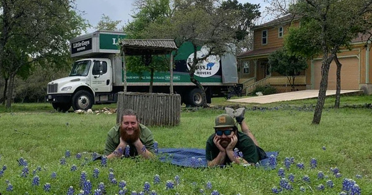 Two Little Guys Movers lay in a field of Texas bluebonnets; a Little Guys Movers truck is in the background