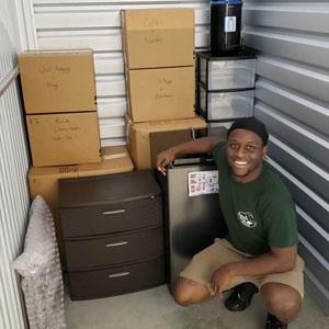A Little Guys mover kneels, smiling, next to furnishings as they are loaded into a storage unit