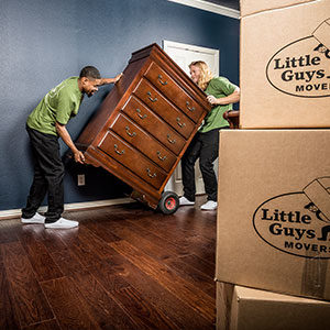 Two movers carefully move a large wooden bureau on a dolly