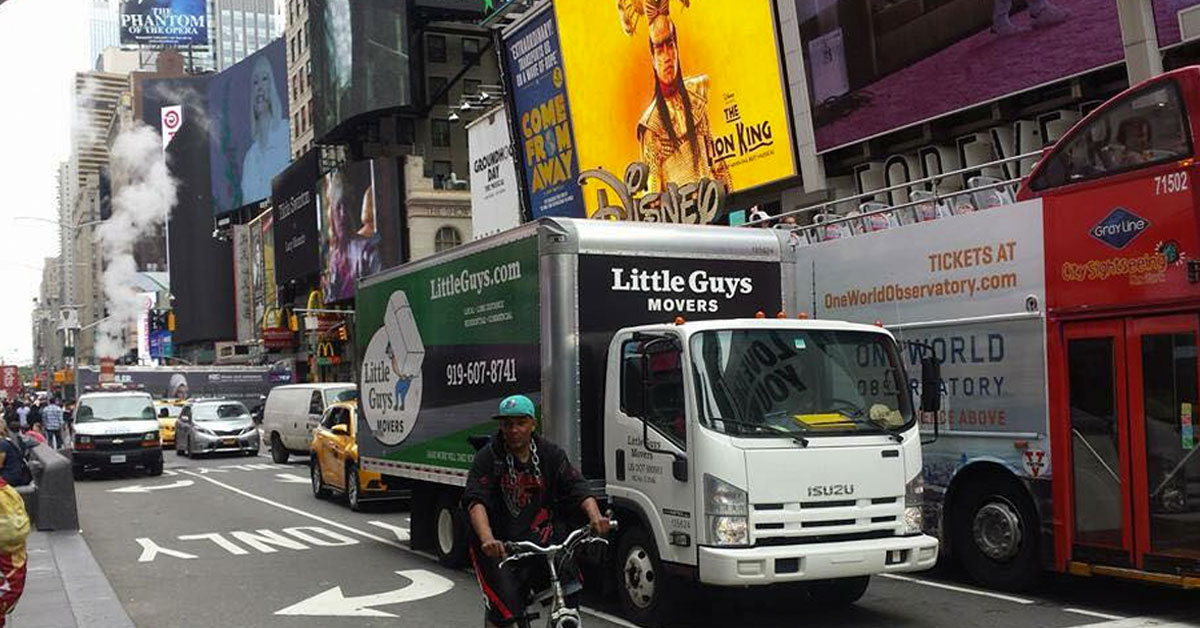 Little Guys Movers moving truck in a busy intersection in downtown Manhattan, NY