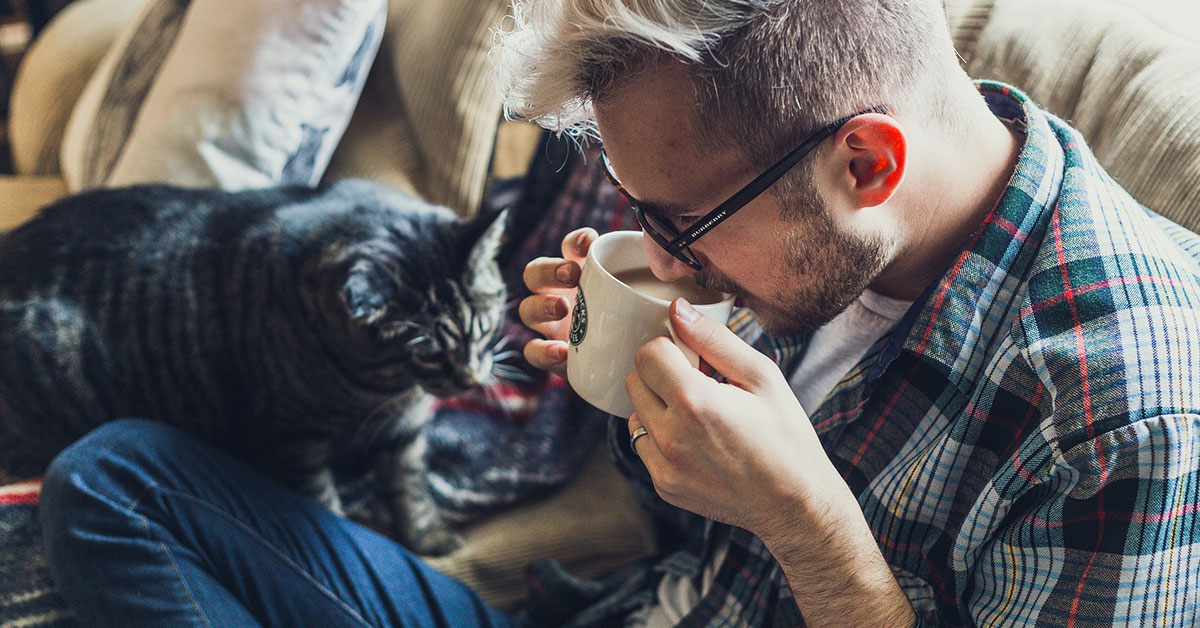 male sipping coffee next to cat
