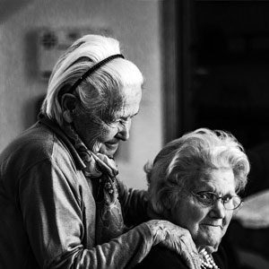 black and white photo of two seniors, one with her hands on the shoulder of her friend