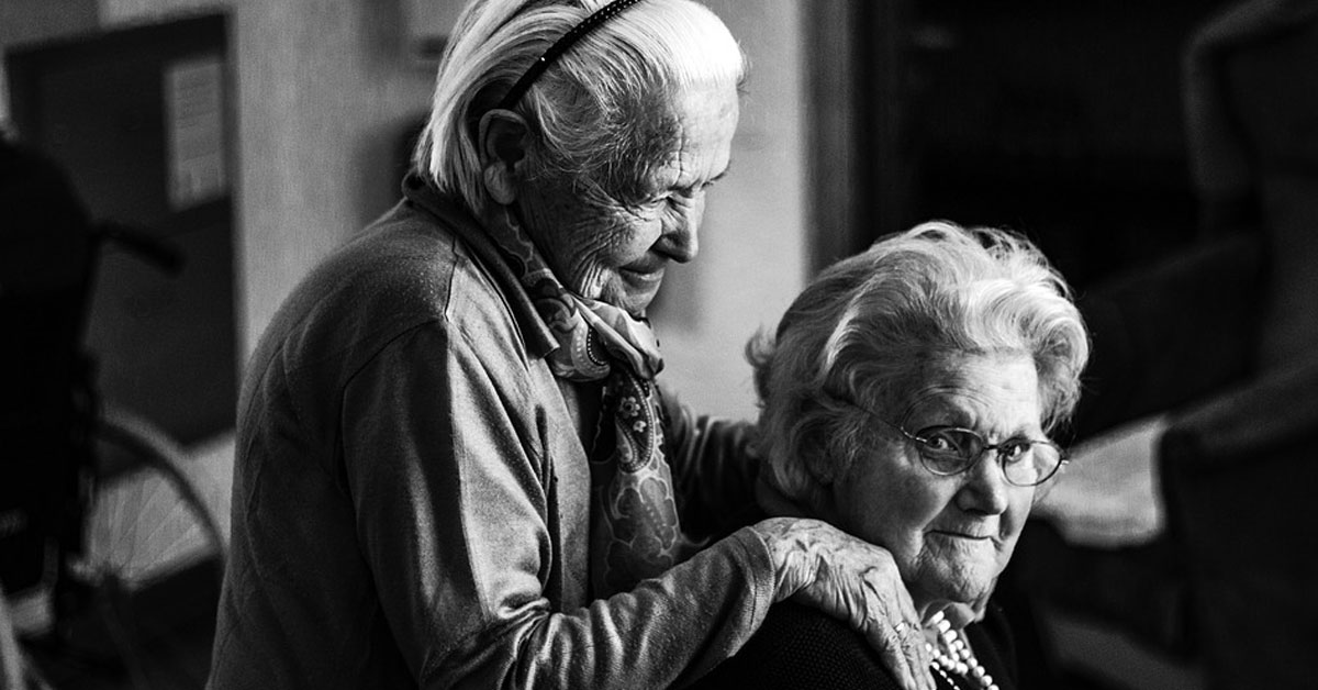 black and white photo of two seniors, one with her hands on the shoulder of her friend