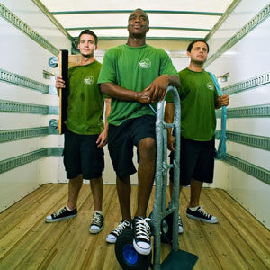 three movers in green shirts pose proudly in a moving truck