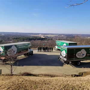 Three moving trucks and a Little Guys Movers moving crew arranged in front of a beautiful outdoor scene.