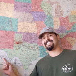 A Little Guys mover smiles and points to a map of the U.S. with a thumbtack marking Lubbock, TX.