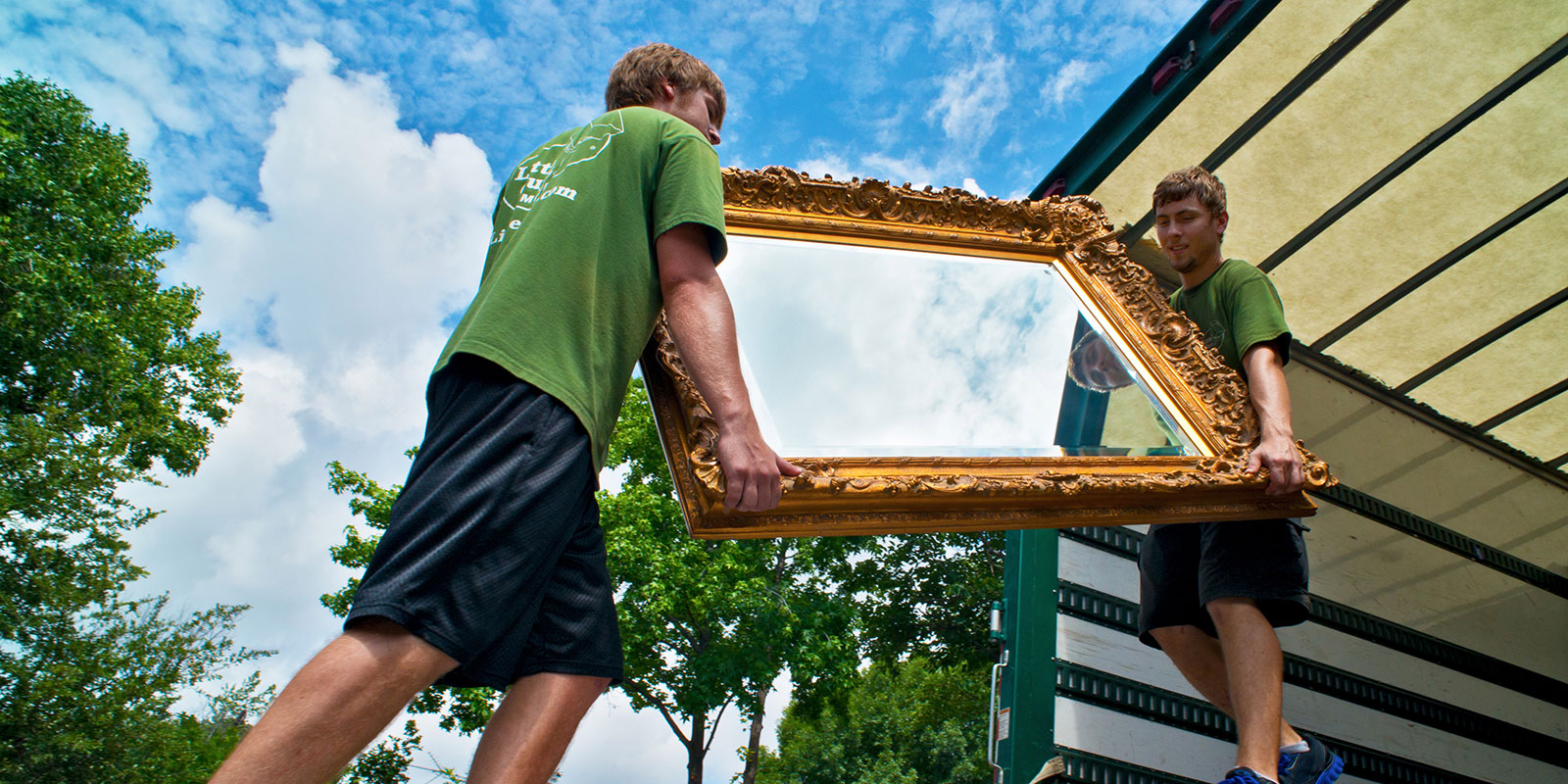 Two Little Guys Movers load a large, decorative mirror onto the moving truck.
