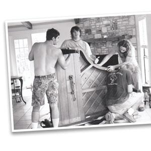 Black and white image of three Little Guys Movers assembling a piano in the nineties.