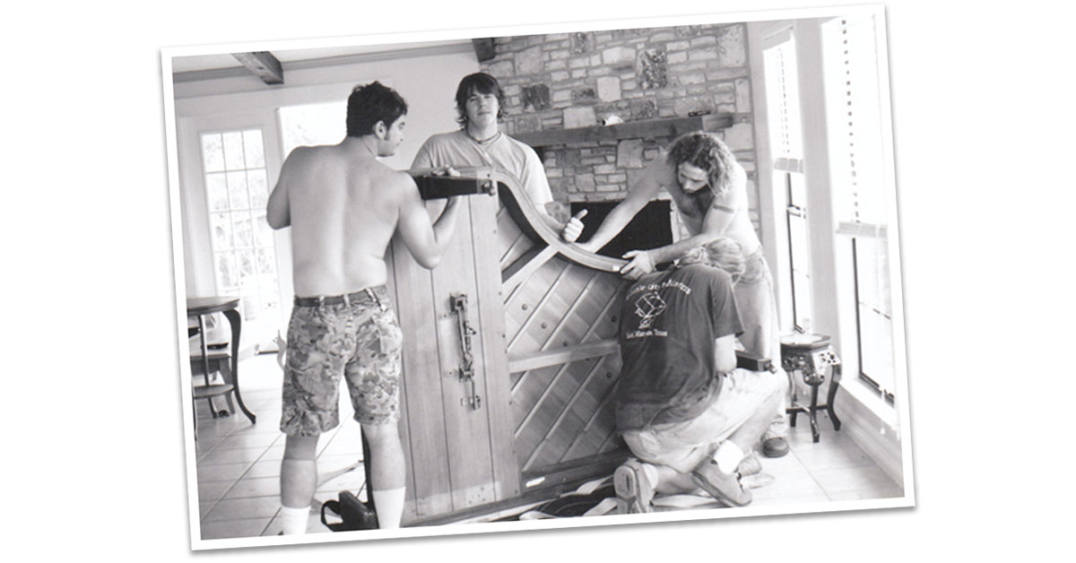 Black and white image of three Little Guys Movers assembling a piano in the nineties.