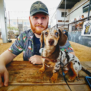 The Lubbock Branch Manager sits at a wooden table with his adorable dappled dachshund.