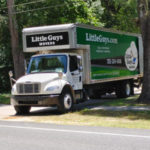 A Little Guys Movers moving truck pulls out of a tree-covered driveway in Alachua County.
