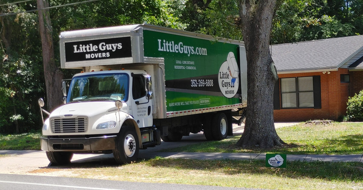 A Little Guys Movers moving truck pulls out of a tree-covered driveway in Alachua County