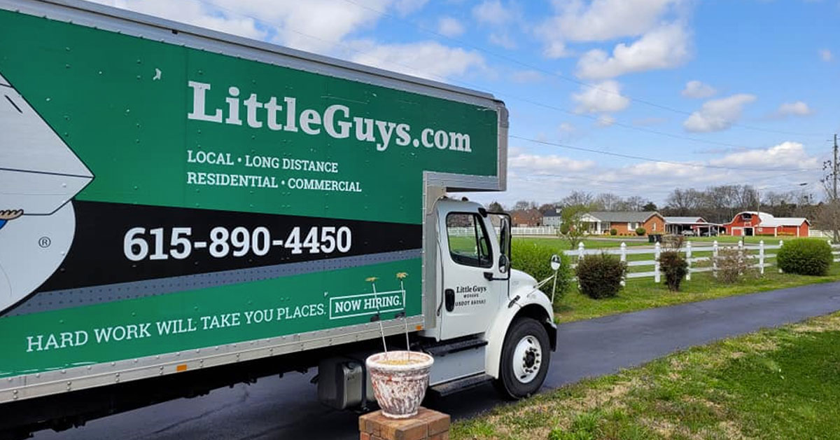 A Little Guys Movers moving truck drives through a Nashville neighborhood