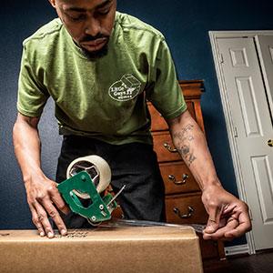 A mover carefully tapes a moving box closed.